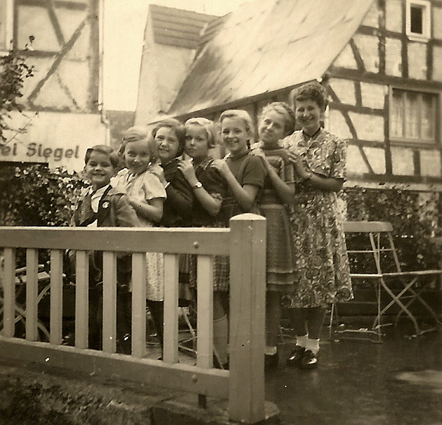 Mädels mit Hahn im Korb am Gasthaus Becker 1951 - Im Hintergrund Metzgerei Siegel und rechts Haus Jakob Buhr 3. von rechts Elisabeth Becker (Pelzer)